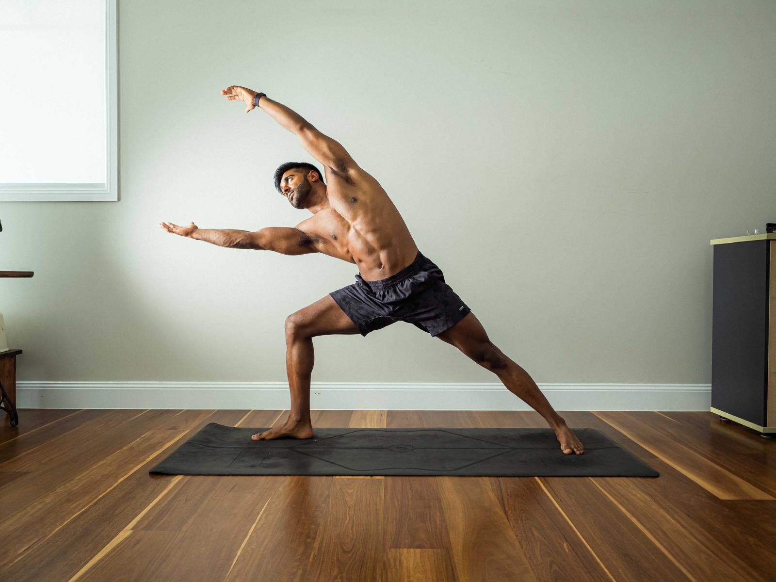 Dr Patel in a side-angle yoga posture, on a wooden floor against a sage wall.